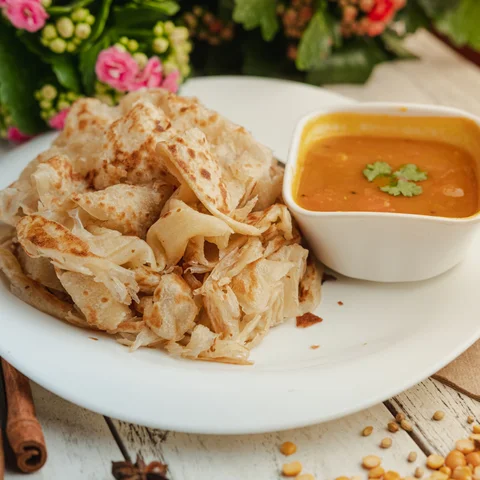 A perfectly layered roti canai served with dal and sambal